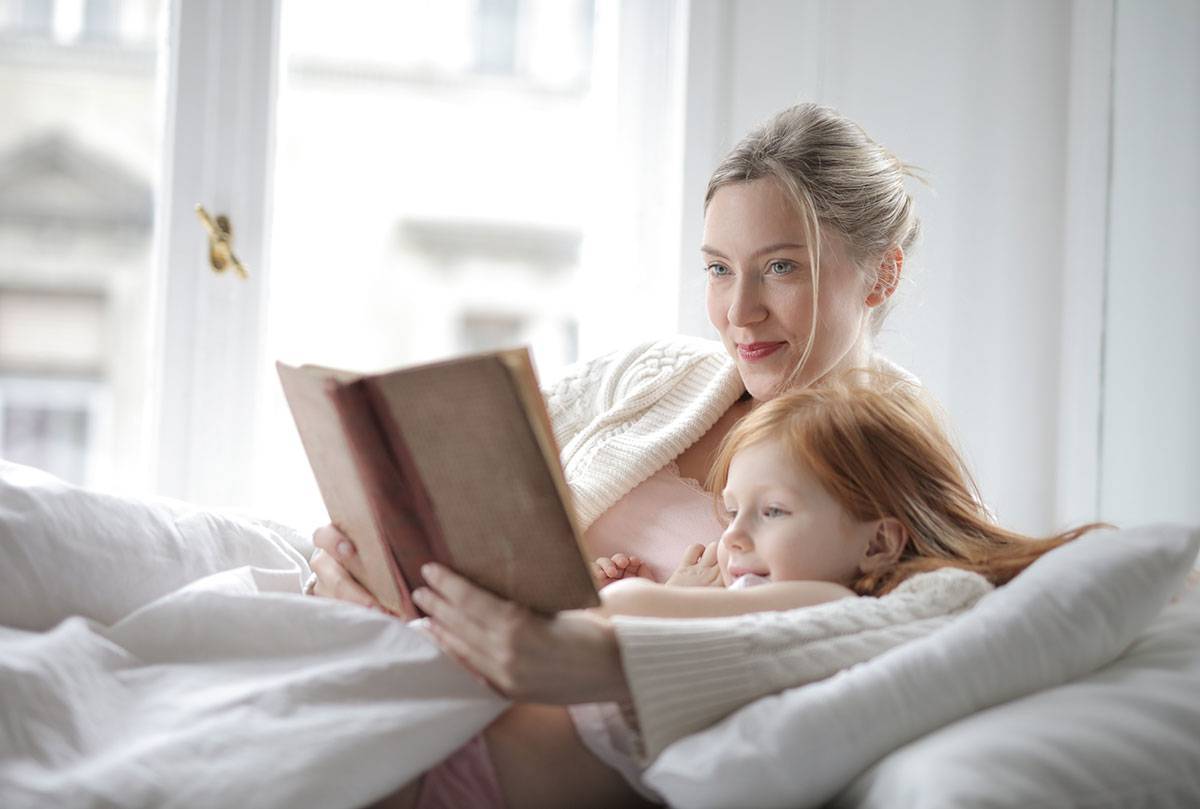 woman in white sweater woman holding book lying on bed