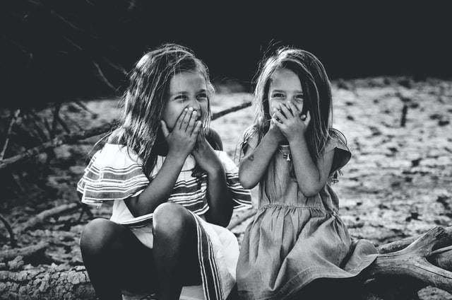 Grayscale photography of two girls closing their mouths