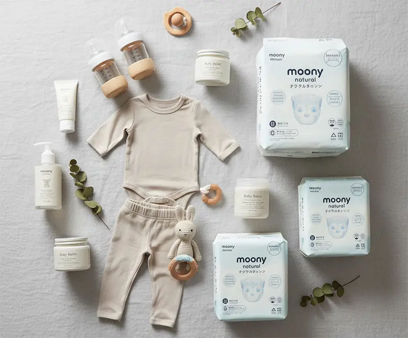 Flat lay of eco-friendly baby essentials — organic cotton clothes, bamboo bottles, natural skincare jars, Japanese packaging — clean minimalist style.